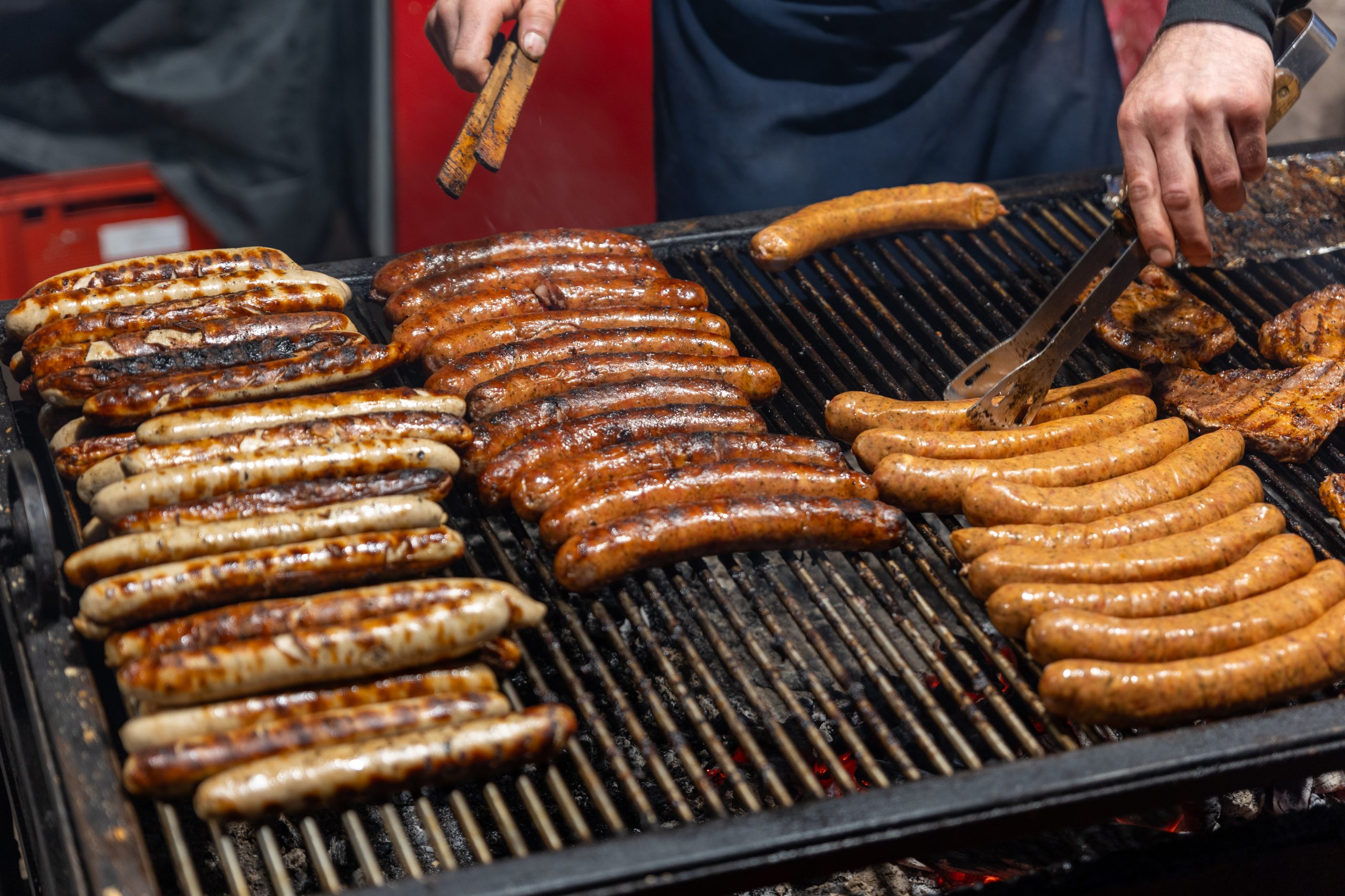 Close-up of juicy bratwurst sausages and meat steaks cooking on grill at German street food market fest